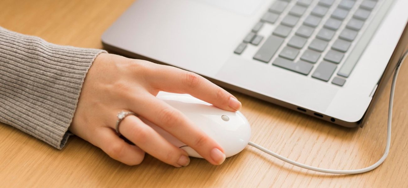 zdjęcie ręki kobiecej na myszce komputera obok laptopa